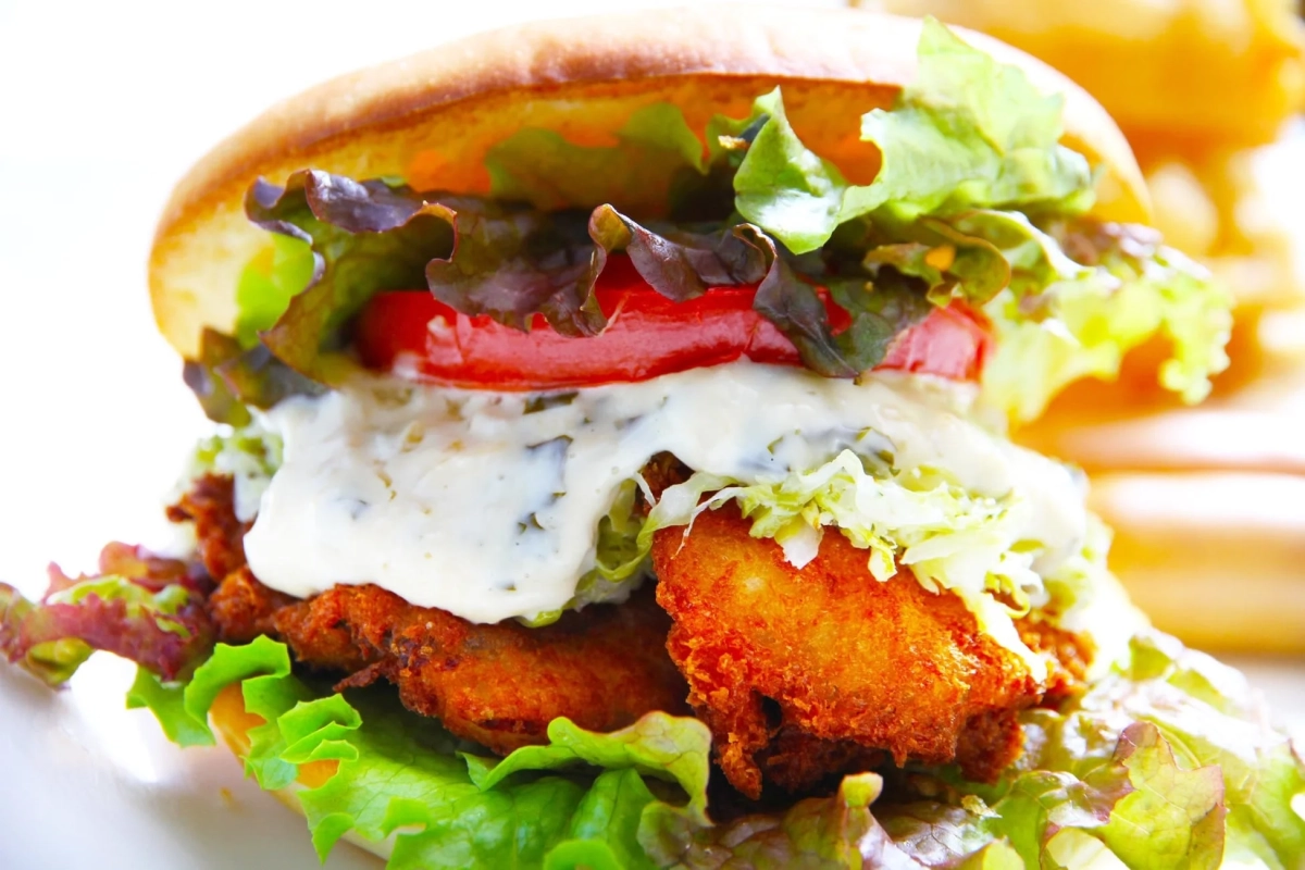 バンズに挟まれた揚げたパティ（フィッシュまたはチキン）、レタス、トマト、そしてクリーミーなタルタルソースがたっぷりかかったハンバーガー
