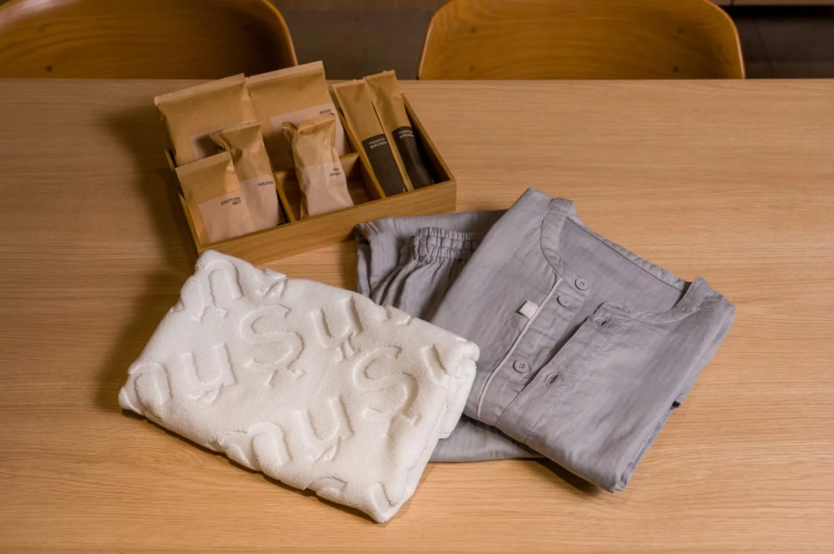 木製のテーブルの上に、グレーのパジャマ、白いタオル、そしてアメニティが入った木箱が置かれています