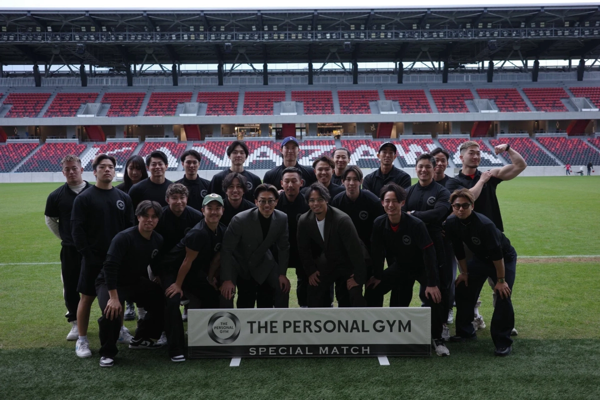 「THE PERSONAL GYM SPECIAL MATCH」のバナーを背景に、多くの人々がスタジアムの芝生に集まり、集合写真を撮っています