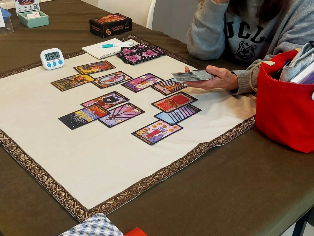 タロットカードが広げられたテーブルで、一人がカードを手にしています。
