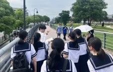 制服を着た学生が川沿いを歩く様子