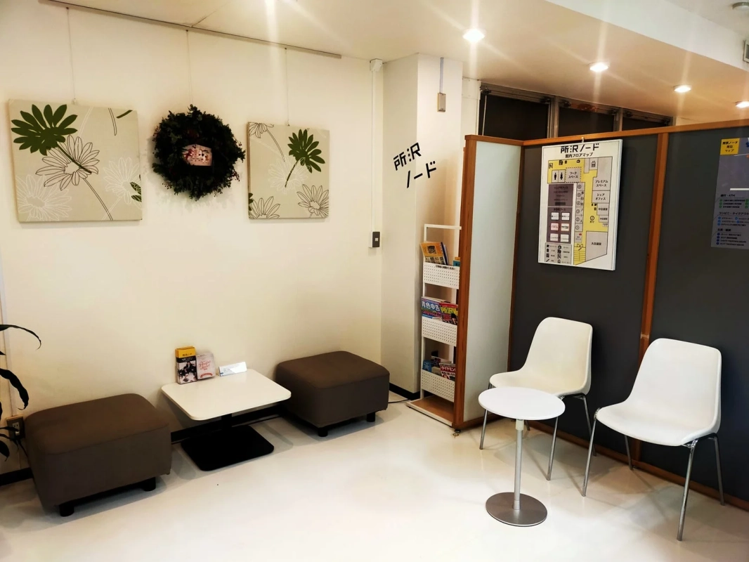 所沢ノードという施設の待合室またはラウンジの様子。壁には花のアートとリースが飾られ、雑誌棚やフロアマップがあります。