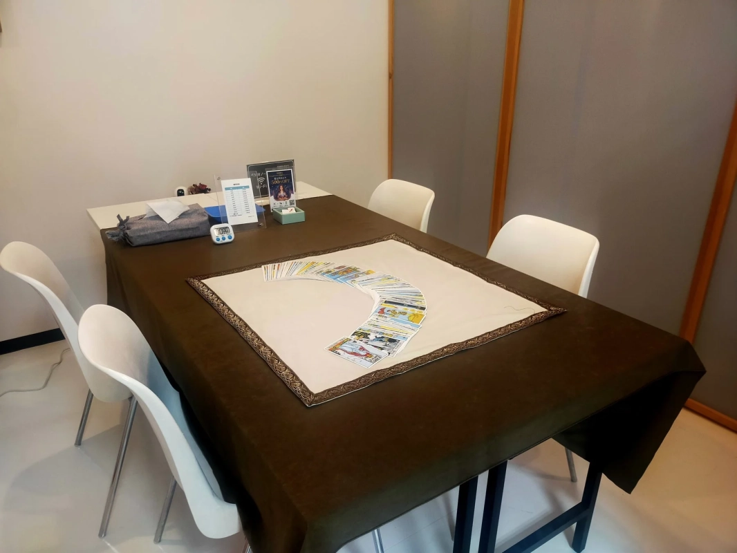 タロットカードが扇状に広げられたテーブルと白い椅子が並ぶ部屋の様子です。