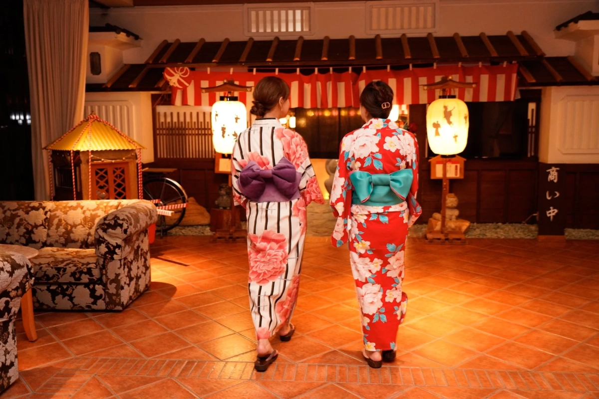 花柄の浴衣をまとった二人の女性が、和風の趣ある室内を歩いている後ろ姿