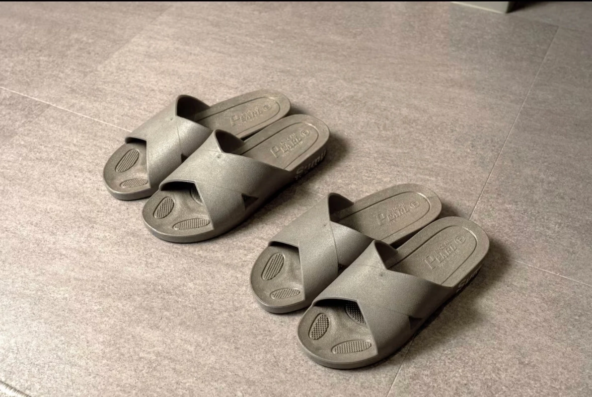 グレーのシンプルなサンダルが2足、灰色のタイル張りの床に並べられています