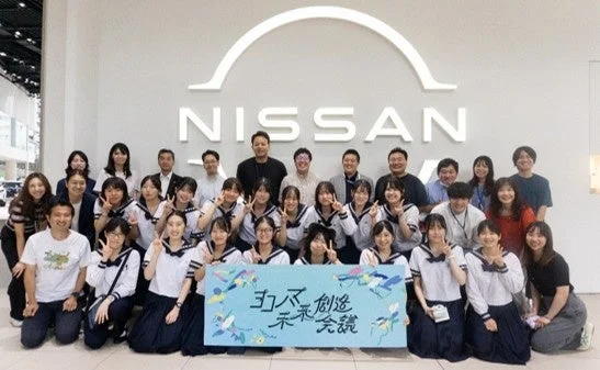 日産自動車のロゴの前で集合写真