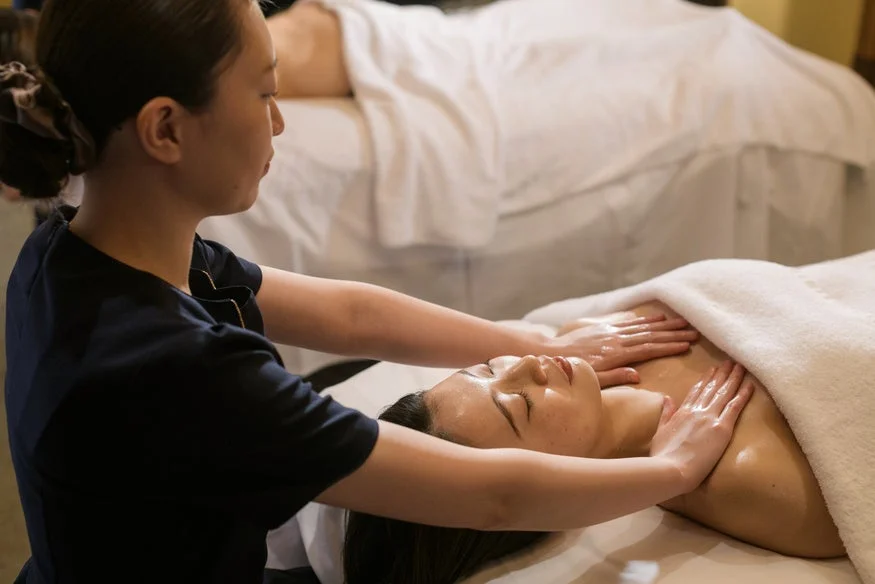スパやエステサロンで、セラピストの女性が顧客の胸元にオイルを塗布しながらマッサージを施している様子