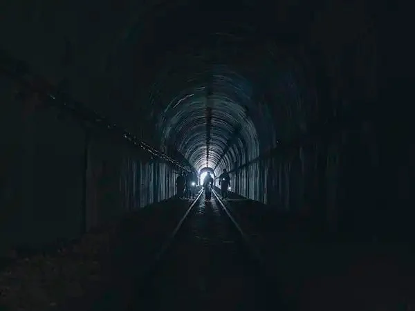 暗い鉄道トンネルの奥に強い光が見え、数人の人影がその光に向かって歩いている