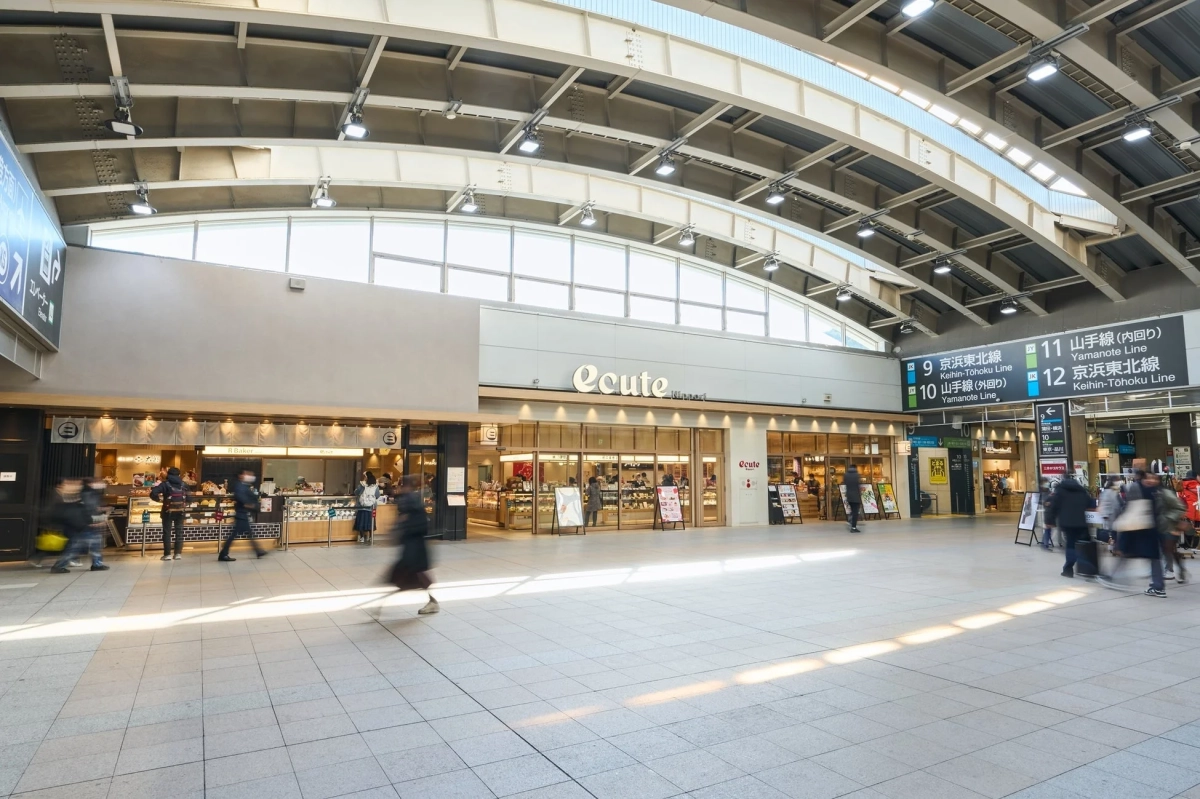広々とした駅構内の様子。ecuteやR Bakerなどの店舗が並び、多くの人が行き交っている。山手線や京浜東北線の案内表示が見える、明るく現代的な駅の風景。