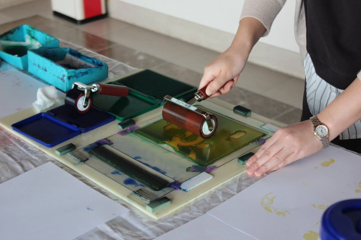 一人の人物が版画制作を行っており、ローラーを使って版にインクを塗っている様子