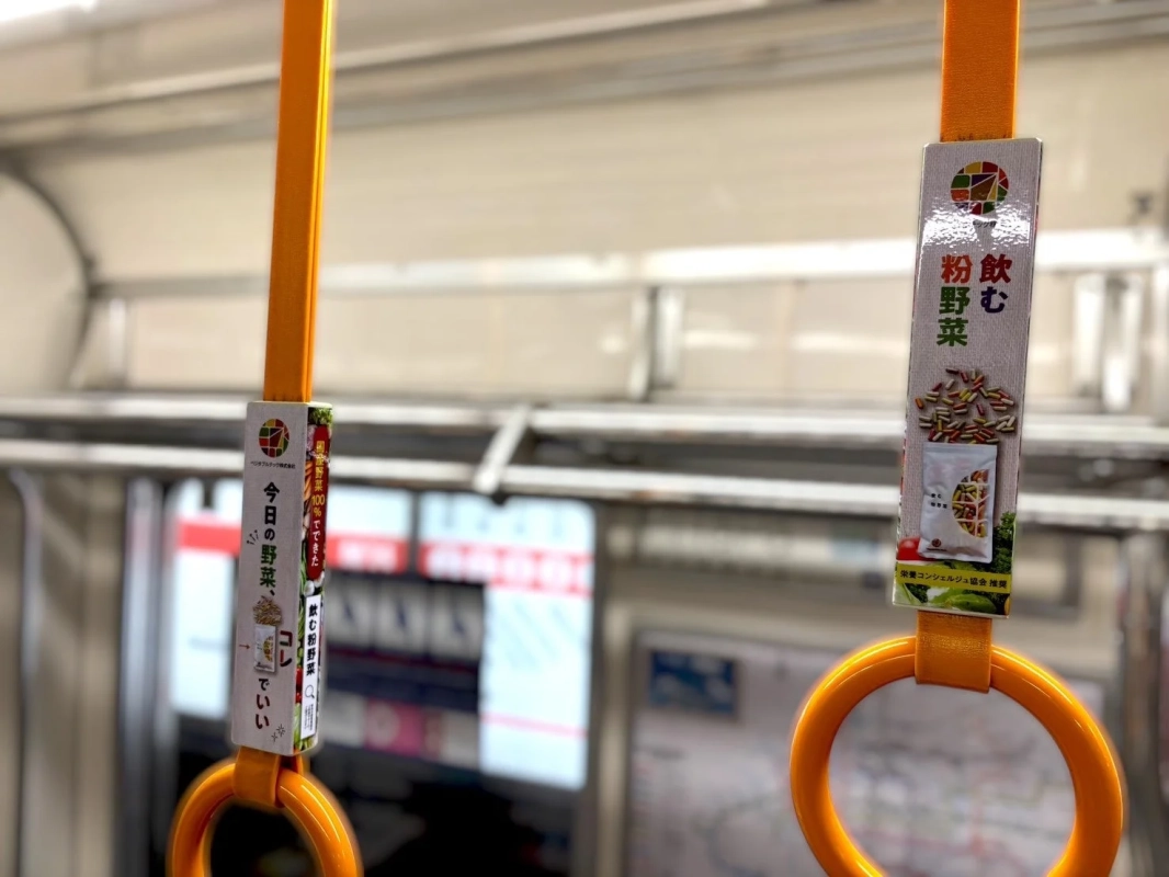 電車内の吊り革に設置された「飲む粉野菜」の広告