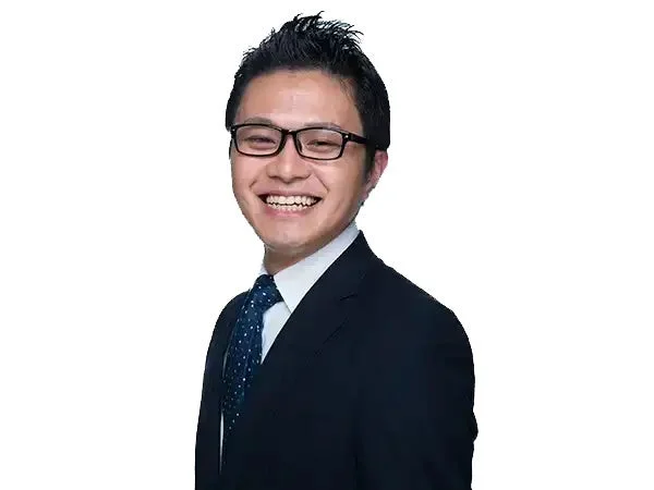 黒いスーツとメガネを着用したアジア系の男性が、明るい笑顔を見せているポートレート写真