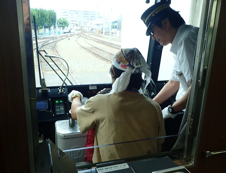電車の運転席で指導を受けながら運転体験をしている様子