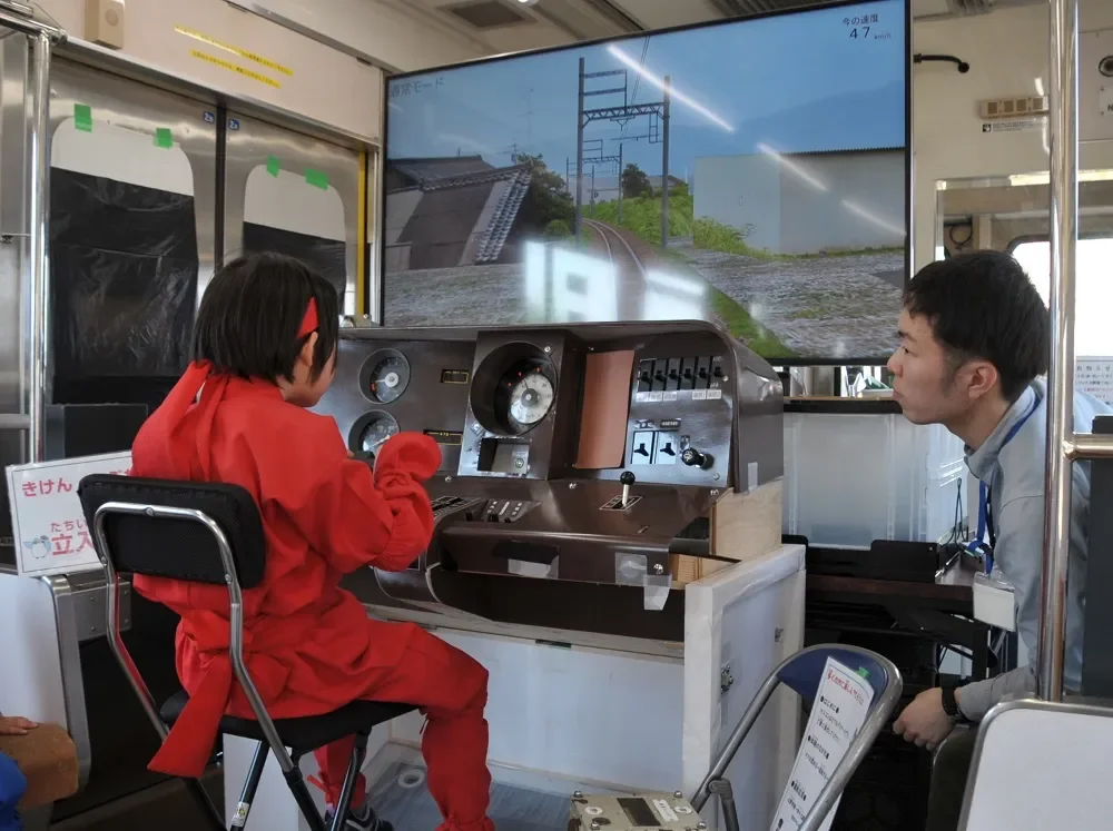 赤い衣装を着た子供が鉄道運転シミュレーターを操作している様子