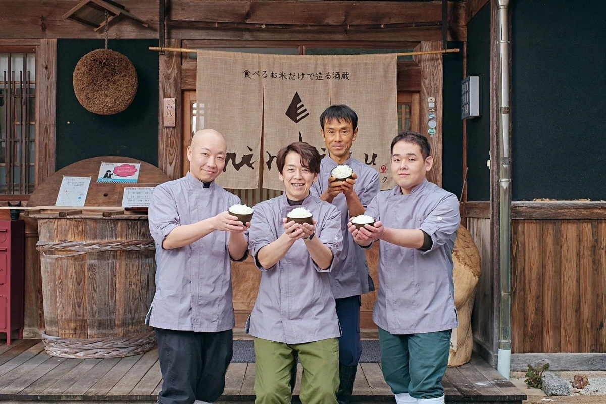 酒蔵を背景に白米の入ったお椀を掲げる男性たち