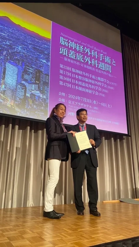 「脳神経外科手術と頭蓋底外科週間」のイベントで、ステージ上で男性が女性から表彰状のようなものを受け取っている様子