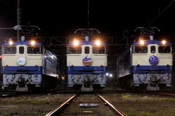 夜の鉄道駅または車両基地で、3台の電気機関車が並んで停車している様子。それぞれの機関車はヘッドライトを点灯させ、暗闇にその姿を浮かび上がらせています。