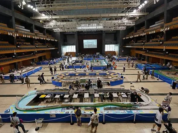 広大な屋内ホールで鉄道模型の展示会が開催されており、多くの来場者が精巧なジオラマや模型列車を鑑賞しています