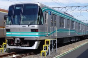 銀色の車体に水色のラインが入った電車が、駅の線路に停車している様子