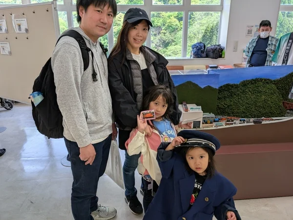 鉄道模型のジオラマが展示された屋内で、家族4人が記念撮影