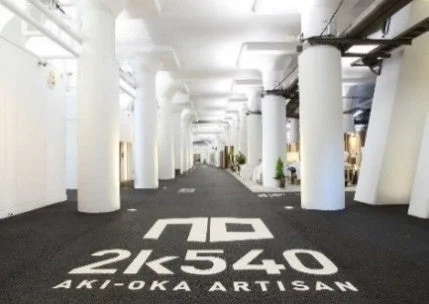 白い柱が並ぶ長い屋内通路で、床には「2K540 AKI-OKA ARTISAN」という施設名が大きく表示されています。