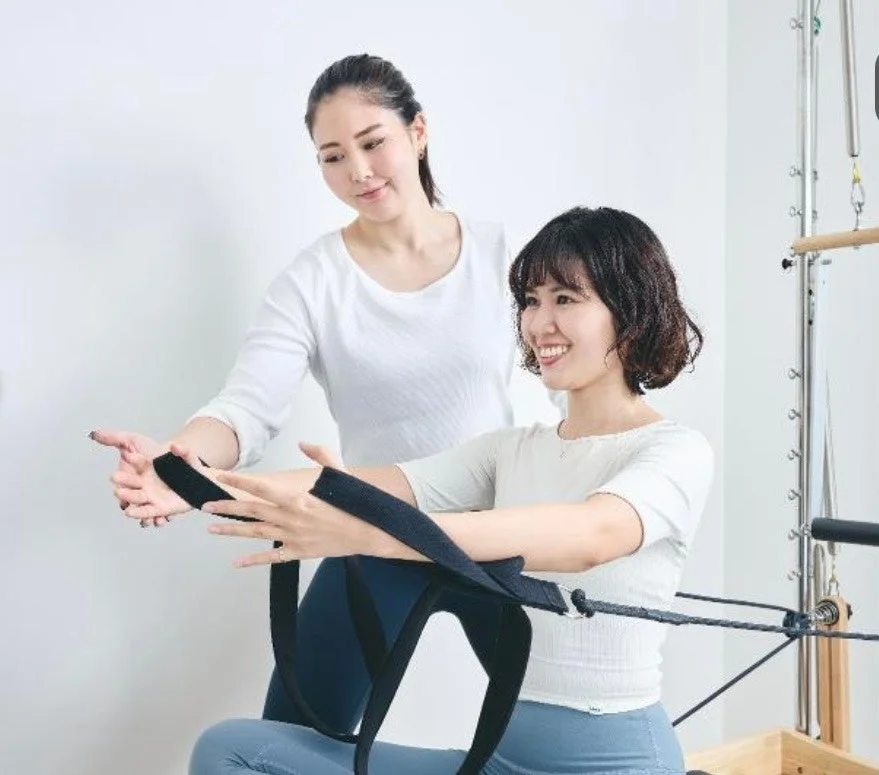 ピラティススタジオで、インストラクターが女性の生徒にリフォーマーを使ったエクササイズの指導をしている様子