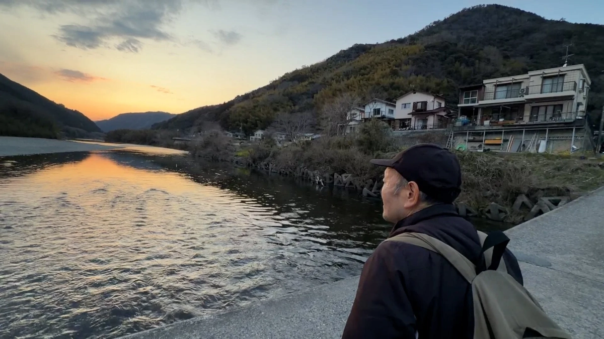 夕暮れの川岸に立つ男性