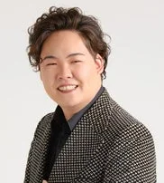 笑顔でカメラを見つめる、黒いシャツと格子柄のジャケットを着用したアジア系の男性のポートレート