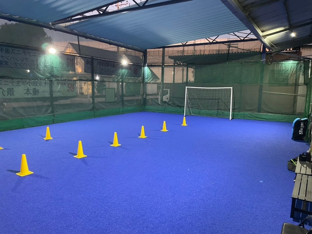 青い人工芝の屋内フットサルコートで、サッカーゴールと複数の黄色いトレーニングコーンが設置されています