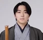 和服姿の日本人男性が尺八のような竹製の楽器を肩に立てて持ち、カメラを見つめているポートレート写真