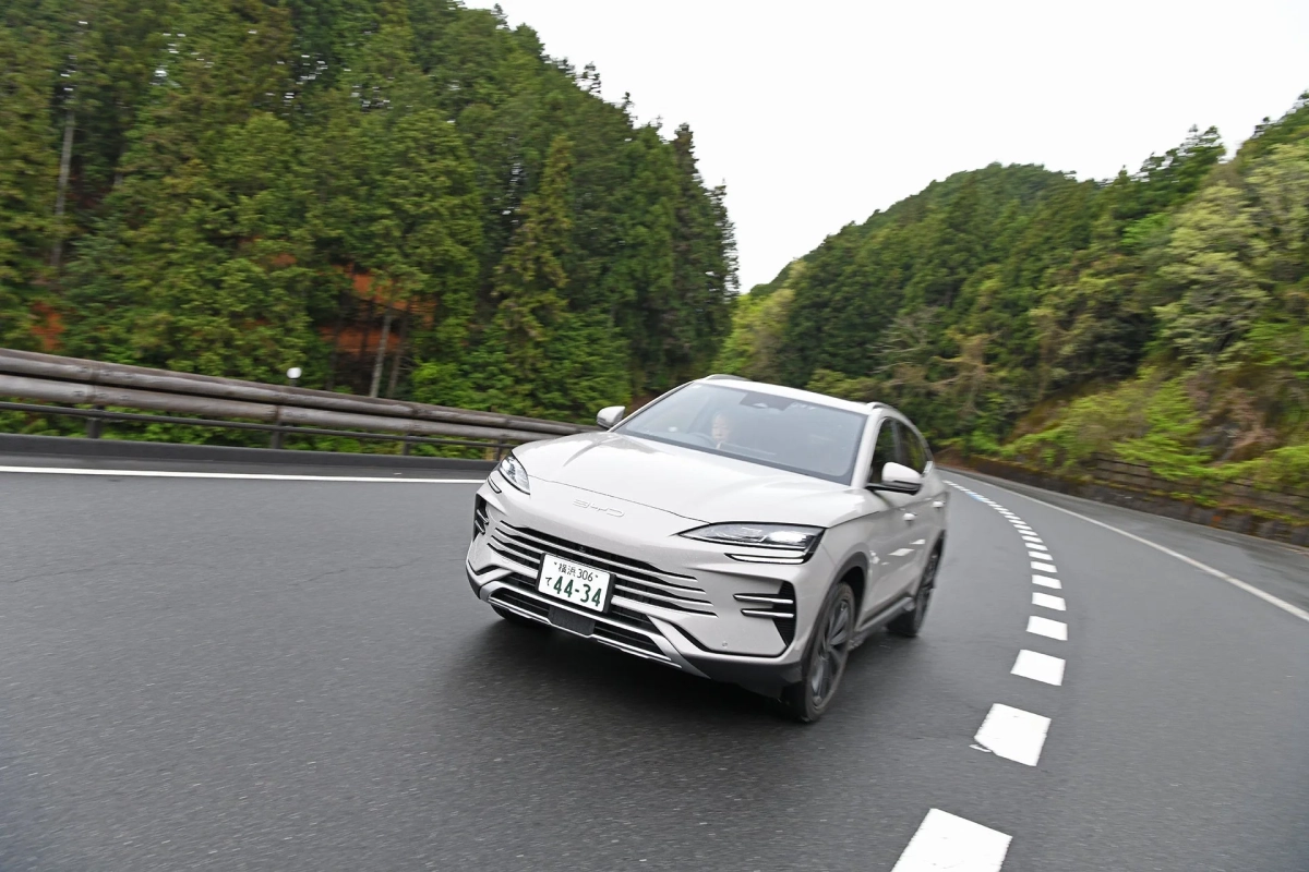 緑豊かな山々が広がるワインディングロードを走行中の白いBYD製SUV