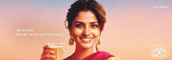 満面の笑みを浮かべたインド人女性がチャイラテのグラスを手にしている広告