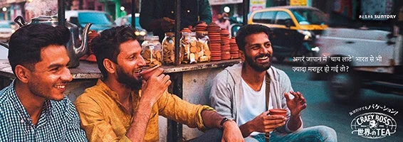 インドの路上で3人の男性がチャイを飲みながら笑顔で談笑している広告