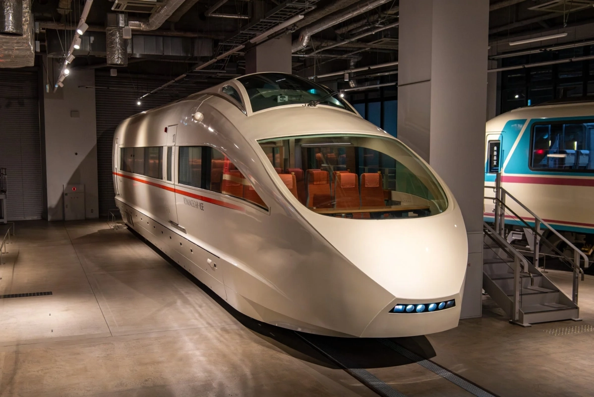 流線型の白いロマンスカーVSEが屋内に展示されており、大きな窓からオレンジ色の展望席が見えます。