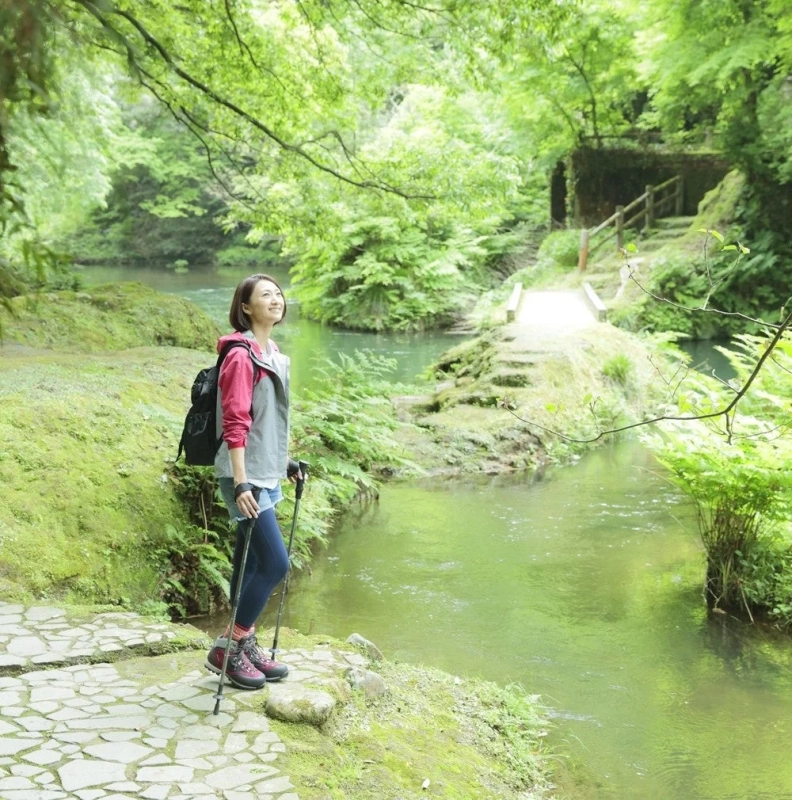 新緑の渓流沿いを歩く女性