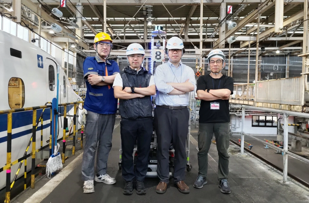 新幹線の整備工場で、ヘルメットを着用した4人の男性作業員が腕を組んでポーズをとっている。