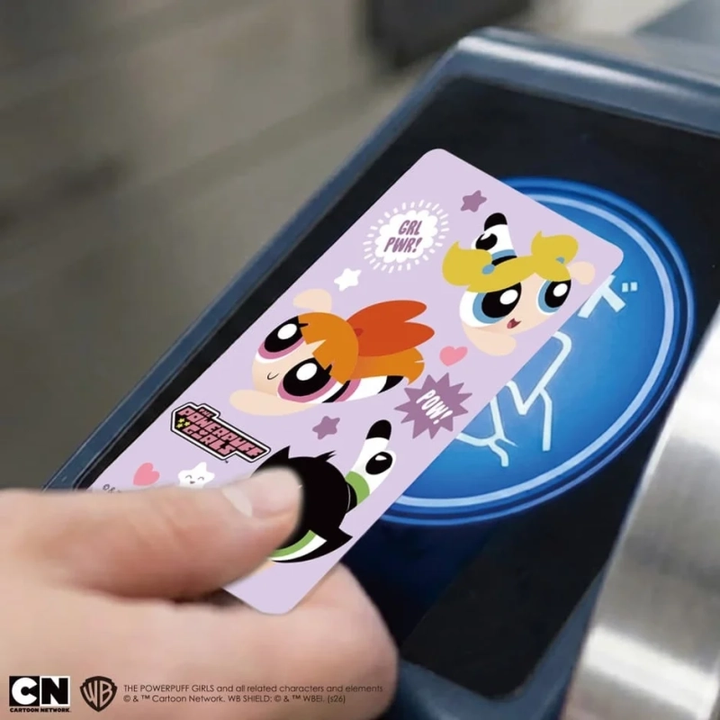 パワーパフガールズのキャラクターがデザインされたカードを、手が駅の改札機のような端末にかざしている様子です。カードにはブロッサム、バブルス、バターカップが描かれており、ポップなデザインが特徴です。