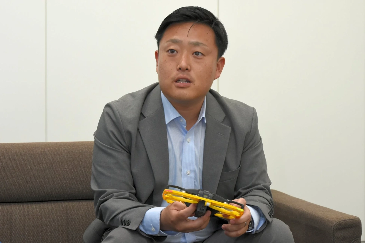 スーツ姿の男性がソファーに座り、小型のドローンのようなデバイスを手に持っています