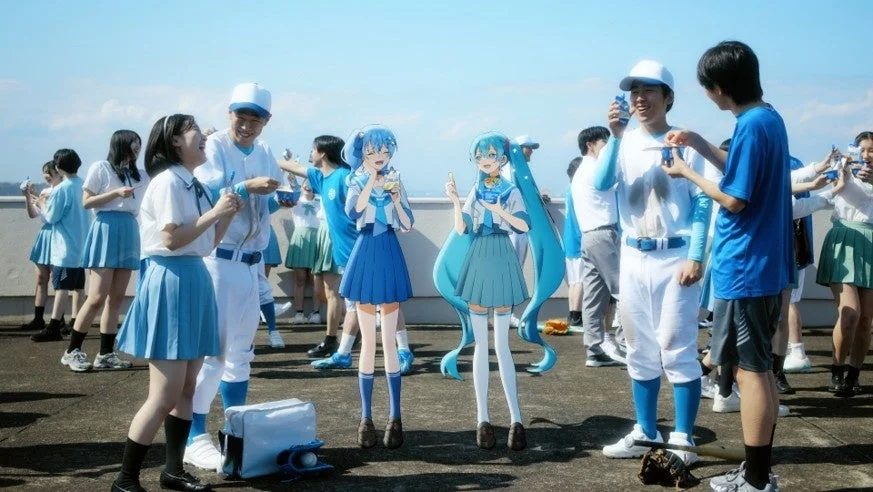 屋上で楽しそうに交流する学生たちと、初音ミクのようなバーチャルアイドルが描かれた画像です。野球部員や制服姿の生徒たちが青いドリンクを手にしています。青春を感じさせる爽やかな雰囲気です。