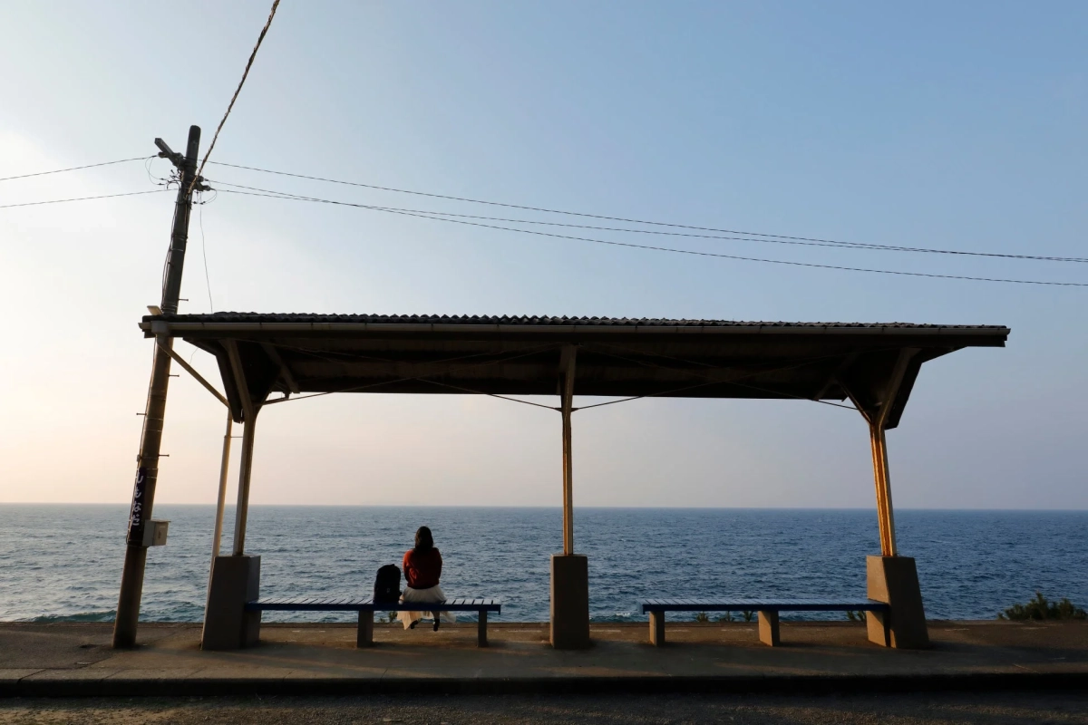 海辺の待合室で、一人の女性が穏やかな海を眺めている風景