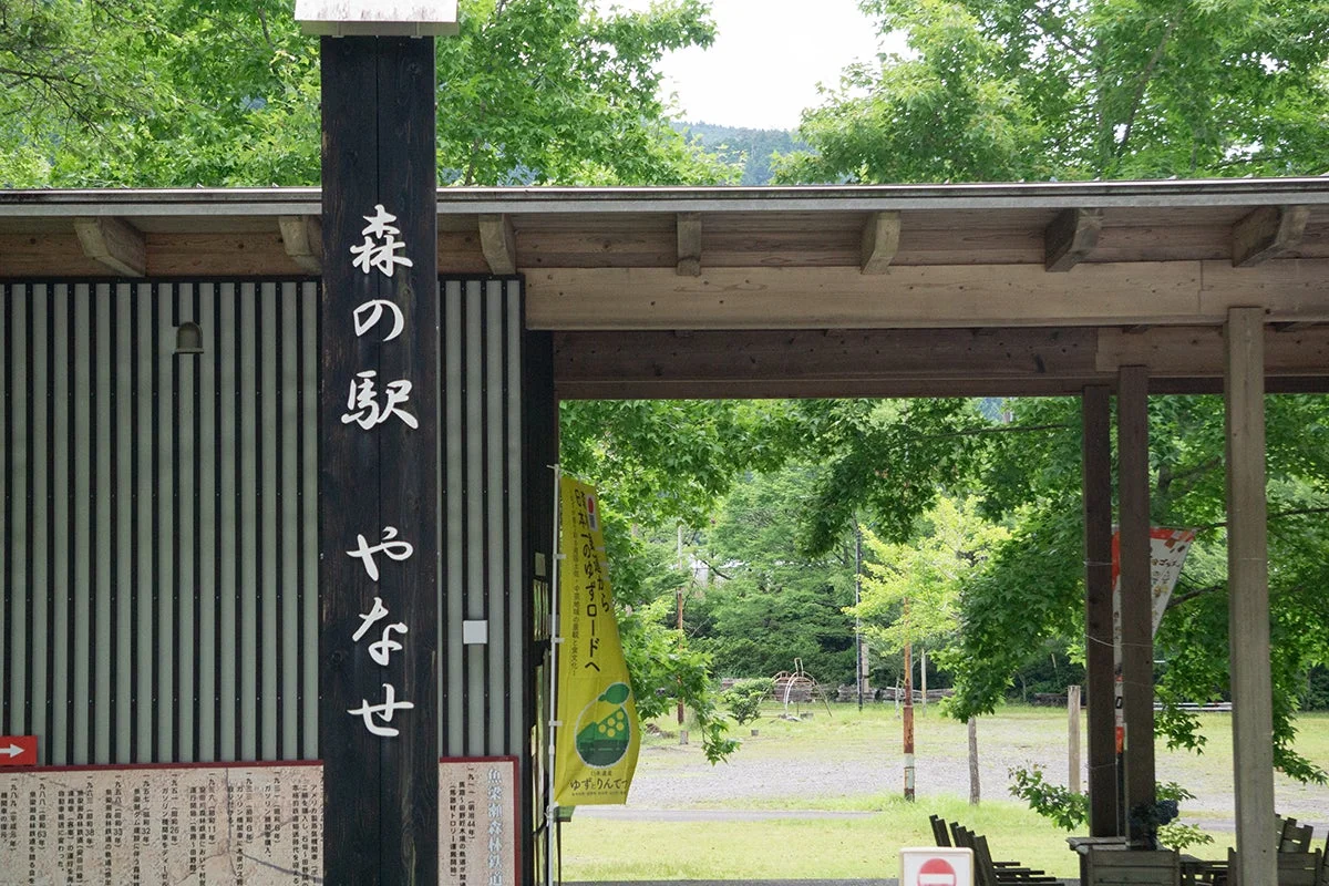 「森の駅 やなせ」の入り口付近を捉えた写真。木製の看板に駅名が示され、横には「ゆずロード」を案内する黄色い旗が立っている。