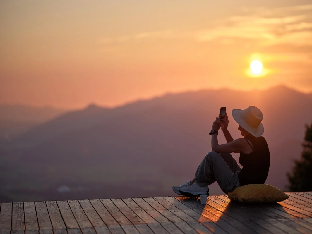 夕焼けの山々とスマホを構える人物