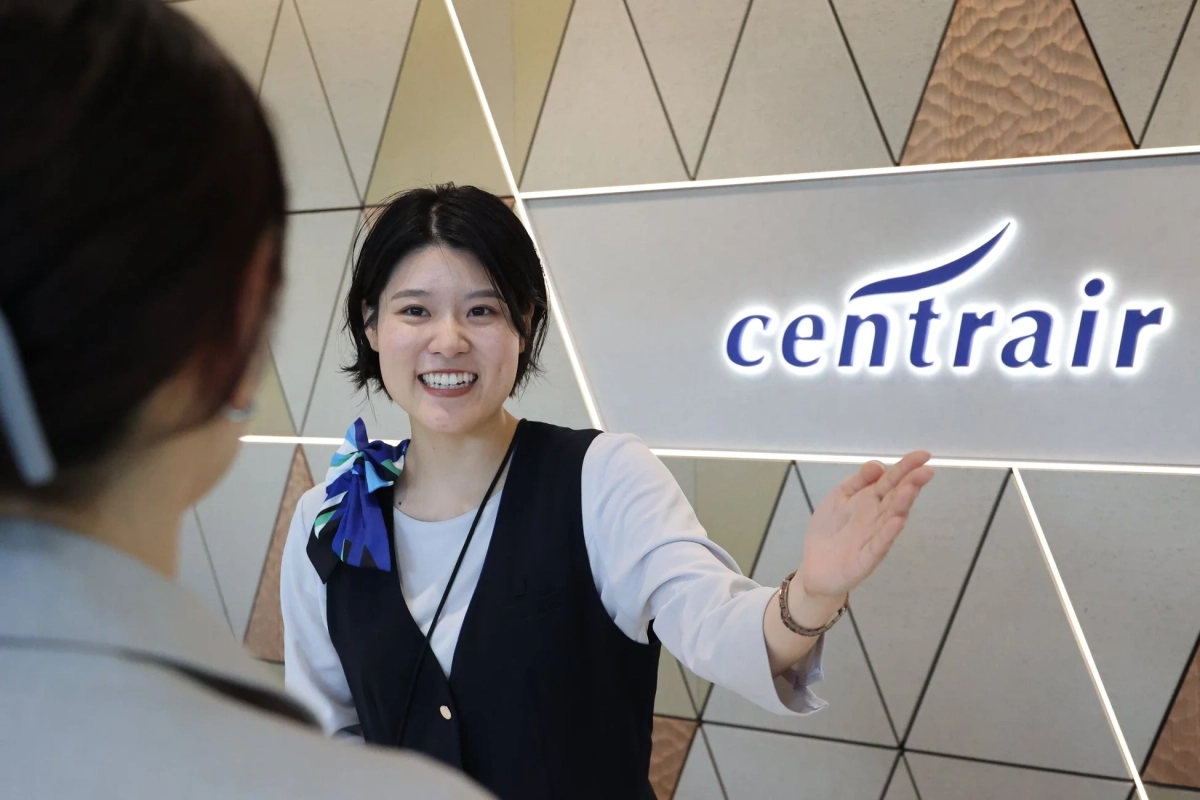 空港の受付で、制服を着た女性スタッフが笑顔で来客を案内している様子
