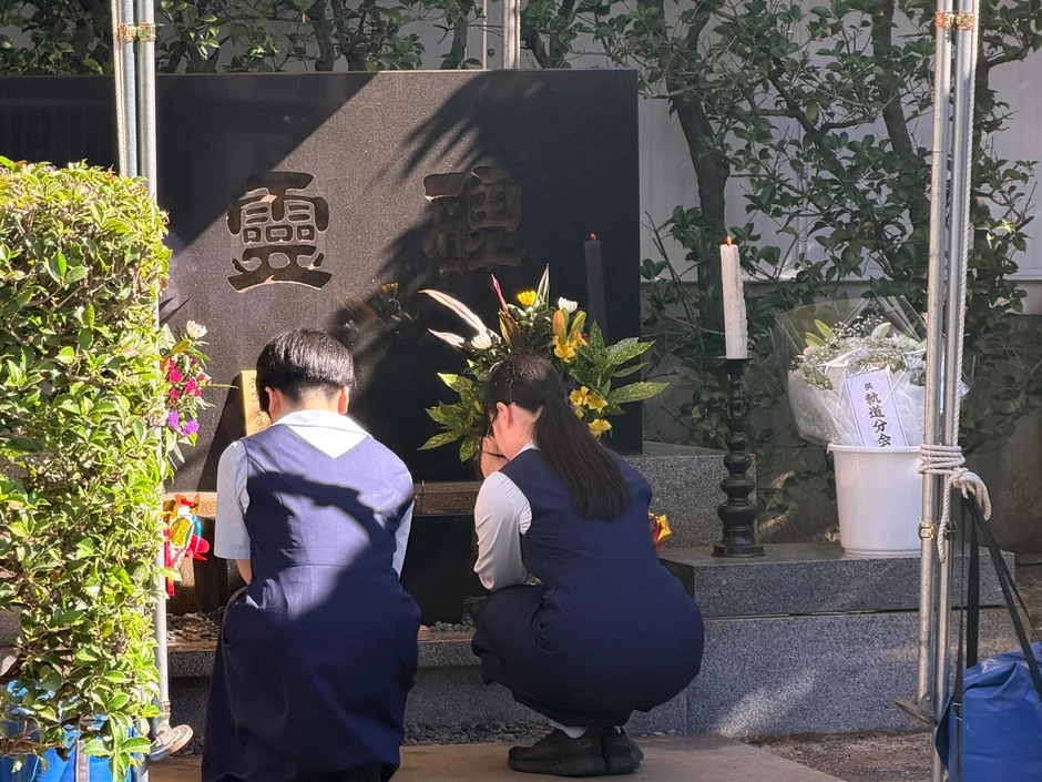 慰霊碑の前で手を合わせる制服姿の生徒