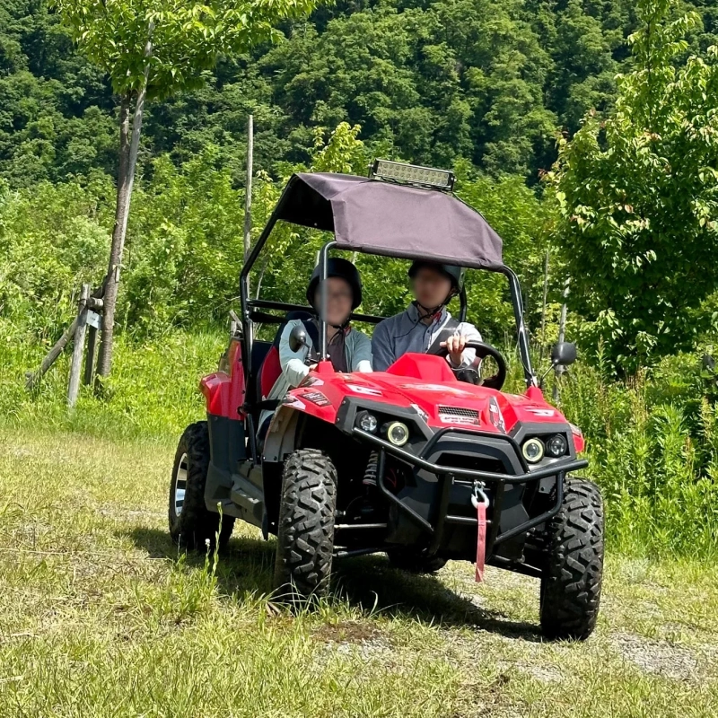 赤いオフロード車に乗った2人が森の中を運転している様子