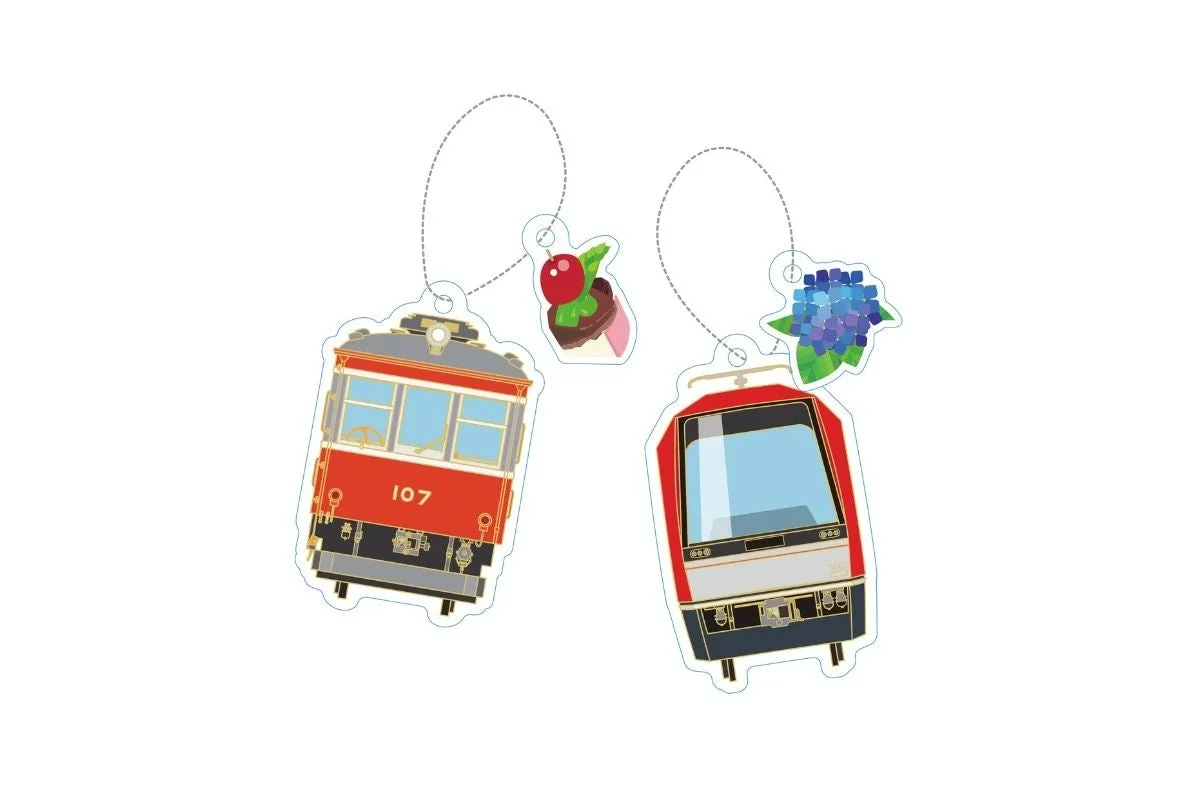 2種類の電車型キーホルダーが並べられています。1つは「107」の番号が入ったレトロな赤い電車で、チェリーケーキのチャームが付いています。もう1つは現代的な赤い電車で、青い紫陽花のチャームが付いています。