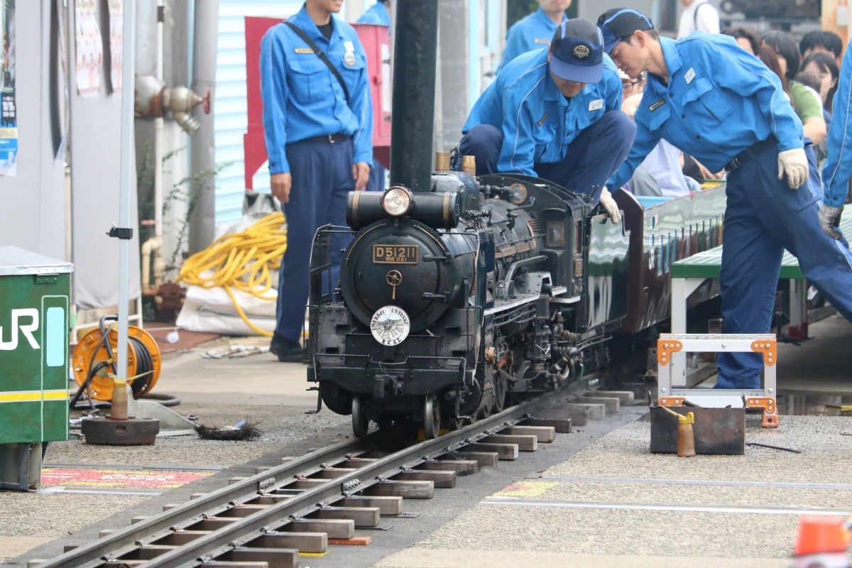 青い制服を着たスタッフがミニチュアのD51形蒸気機関車を点検している様子