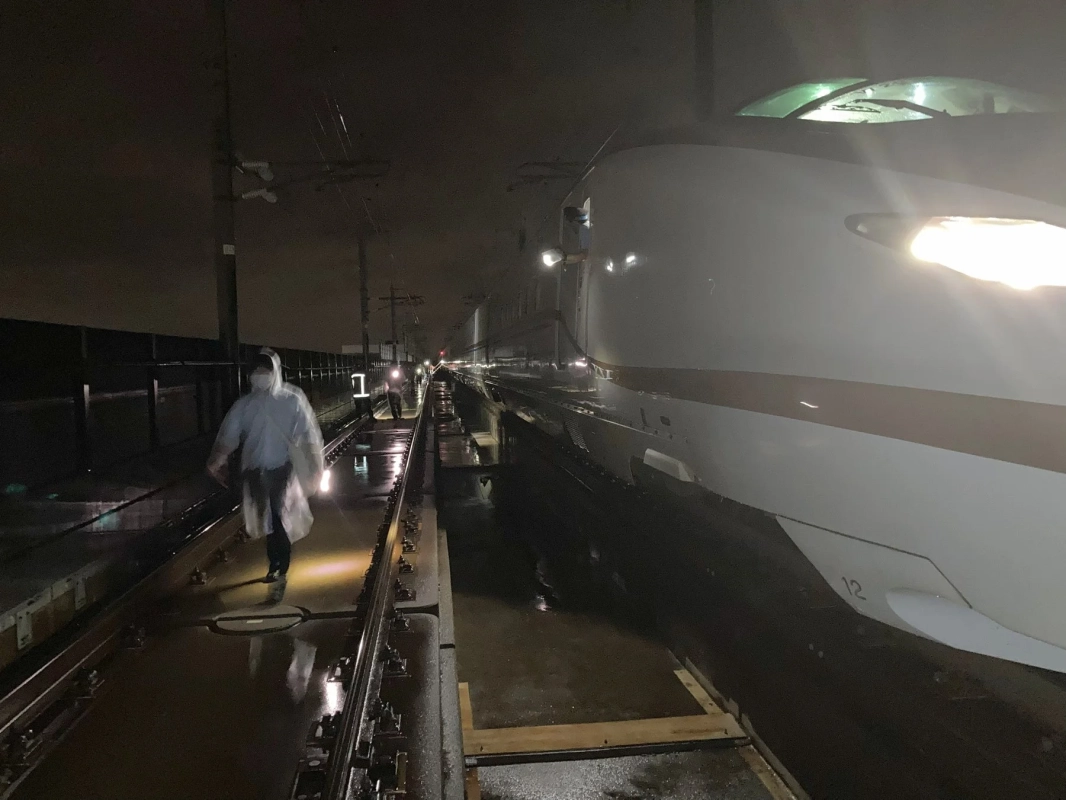 夜間の線路を歩く作業員と停車中の新幹線