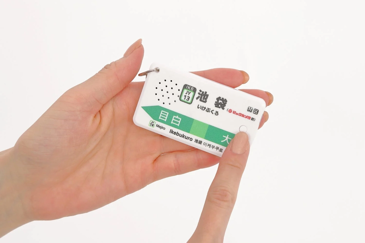 女性が手のひらに、JR山手線の駅名標を模したキーホルダーを握っています