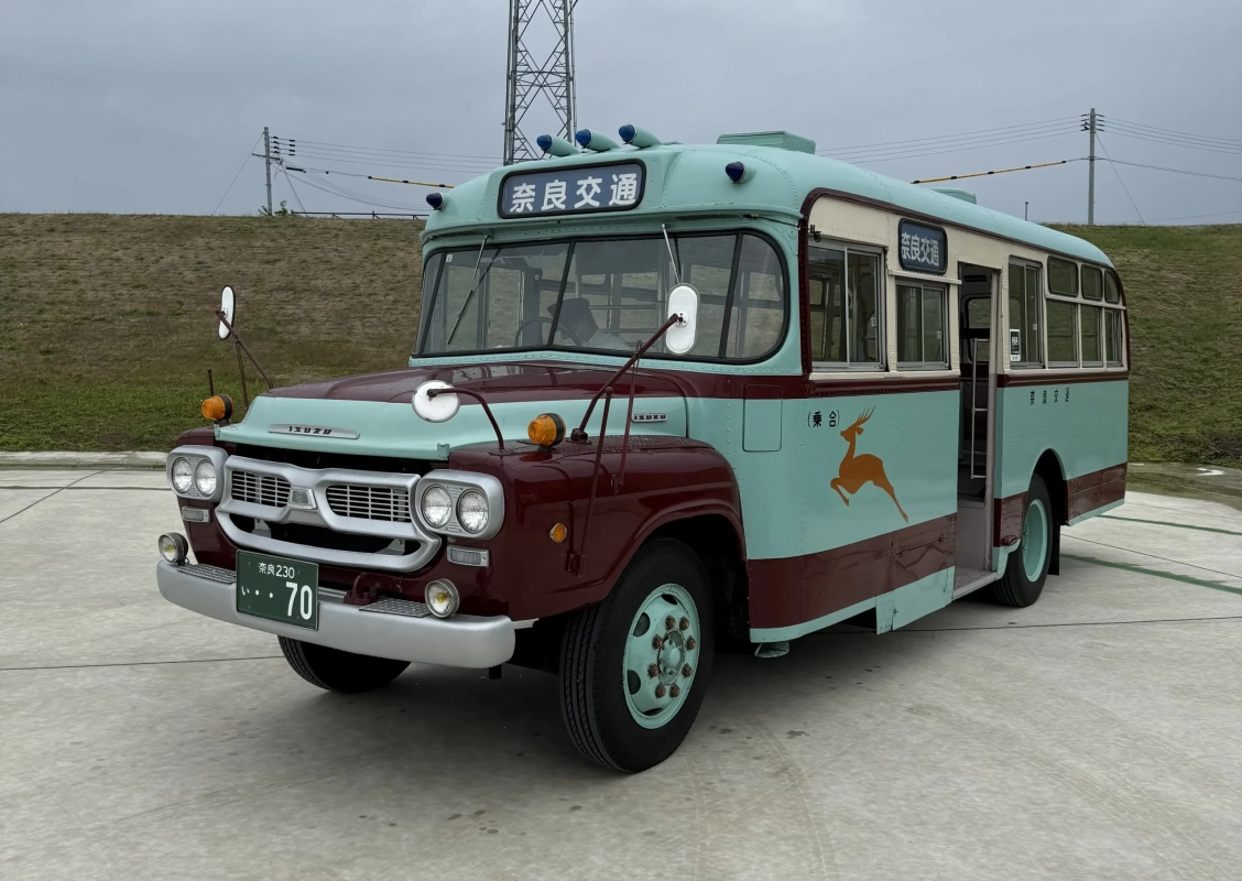 レトロなデザインが特徴的な奈良交通のバスが、屋外のコンクリートの地面に停車している様子です。車体はマルーンと水色のツートンカラーで、側面には鹿のイラストと「乗合」の文字が見えます。